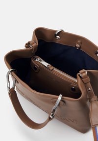 Brązowa skórzana torba o strukturalnym fasonie, z srebrnymi okuciami i granatowym wnętrzem. W środku znajduje się kieszeń zapinana na suwak.