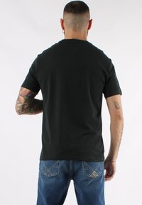 Camiseta de algodón negra de manga corta y escote redondeado, combinada con jeans de denim azules que presentan distintivos bolsillos traseros cosidos.