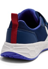 Niebieski but sportowy z siateczkową cholewką, czerwonym uchwytem i białą podeszwą środkową z teksturowaną, fioletową podeszwą zewnętrzną. Zbliżenie na obszar pięty.