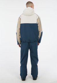 Kleurblokjack met een beige, marineblauwe en witte ontwerp, gemaakt van lichtgewicht stof. Gecombineerd met bijpassende marineblauwe broeken, beide met elastische manchetten.