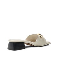 Sandale mule en cuir blanc à motif crocodile, avec un petit talon carré noir et des accessoires dorés. Design à bout ouvert, forme minimaliste.