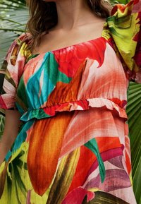 Robe florale colorée en tissu léger, avec un décolleté carré, de courtes manches bouffantes et un ourlet froncé, le tout dans un mélange de couleurs vives.