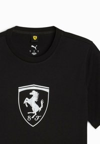 Sorte t-shirt med et hvidt Ferrari-logo, der har en opstaldet hest inde i en skjoldform, mærket med "SF" i bunden.