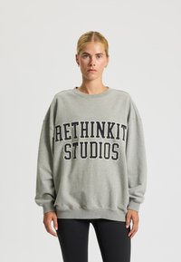 Felpa grigia oversize con "RETHINKIT STUDIOS" stampato in grassetto nero sul petto. Tessuto morbido e polsini a coste.