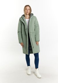 Palton lung, cu glugă, de culoare verde deschis, fabricat din material rezistent la apă. Dispune de două buzunare frontale și închidere cu fermoar. Asortat cu blugi albaștri și adidași albi.