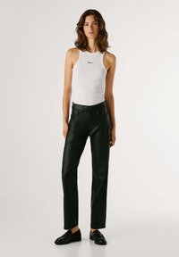 Top a maniche lunghe bianco a costine con logo nero, abbinato a pantaloni in pelle neri a vita alta. Scarpe nere con texture completano l'outfit.