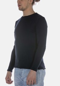 Marineblaue Langarmbluse aus weichem, elastischem Stoff; Rundhalsausschnitt mit rohem Saum; dezentes Nähdetail; kombiniert mit hellblauen Jeans.