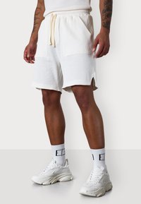 Gerippte weiße Shorts mit einem elastischen Bund, Kordelzug und Seitentaschen. Kombiniert mit weißen Sneakers und strukturierten Crew-Socken.