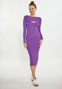Figurbetontes, geripptes Midikleid in lebhaftem Lila, mit langen Ärmeln und einem Cutout vorne. Kombiniert mit weißen Sneakers und einer dezenten Textur.