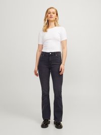 Vaqueros oscuros acampanados de denim, con una cintura ajustada y costuras sutiles. Combinados con una camiseta blanca de manga corta y zapatos negros.