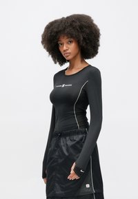 Čierny top s dlhým rukávom a bielym lemovaním, s okrúhlym výstrihom a logom Nike. Nosený s čiernou sukňou z ľahkej tkaniny.