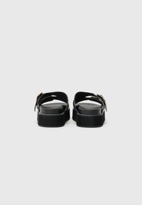 Sandales à plateforme noires avec une finition lisse, présentant une large lanière et une boucle dorée, des coutures sur la semelle et un design à dos ouvert.