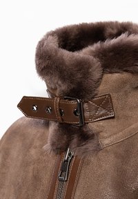 Braune Lederjacke mit einem weichen Pelzkragen, der mit einer Schnalle und einem Druckknopf gesichert ist. Reißverschluss mit einer kontrastierenden glatten Textur.