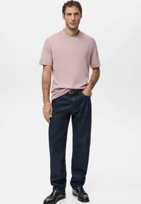 Light pink short-sleeve shirt, relaxed fit. Dark blue straight-leg jeans, paired with black shoes. Simple, clean design with no patterns.