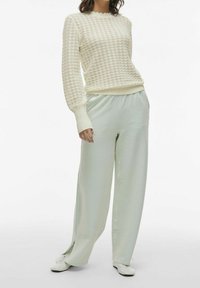 Un pull texturé beige clair avec un motif en nid d'abeille, associé à un pantalon large à carreaux vert menthe. Des chaussures blanches complètent la tenue.