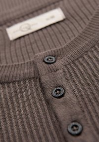 Cardigan de punto acanalado marrón con cierre de botón negro, que presenta una tela texturizada y una pequeña etiqueta cerca del cuello.