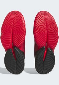 Zapatillas deportivas con suelas de goma rojas y negras que presentan un patrón zigzagueante texturizado para mayor tracción, y una forma aerodinámica para un mejor rendimiento.