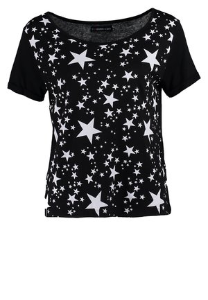 Femme marchant portant un t-shirt noir à motif étoilé, un jean skinny bleu foncé, des bottines noires et portant un sac à main noir.