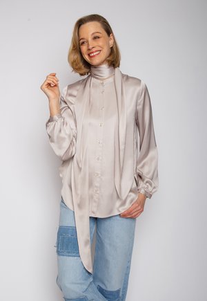 Lange mouw satijnen blouse in licht taupe met een hoge kraag en knopen aan de voorkant, met een lintdetail en een zachte, gladde textuur.