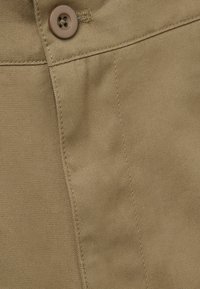 Khaki tkanina s hladkým povrchem. Obsahuje knoflík a viditelné švy podél švů, což zdůrazňuje ušitý design.