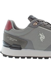 Šedé a červené tenisky U.S. Polo Assn. s texturovanou tkaninou, semišovými akcenty a nápadným logem hrajícího polisty na boku.