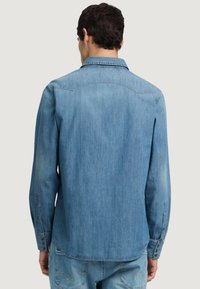 Jeanshemd in hellblauer Farbe, mit langen Ärmeln, Knopfmanschetten und einem klassischen Kragen sowie einem gekrümmten Yoke-Design auf der Rückseite.