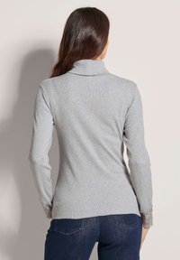 Grijze langemouwen top met een hoge hals, geribbelde textuur en kantaccenten bij de mouwen. Gemaakt met donkere spijkerbroeken, bekeken vanaf de achterkant.