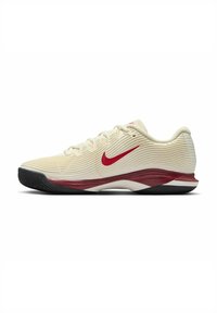 Scarpe da tennis Nike in crema con texture a righe, presentano accenti rossi e una suola in gomma nera. Design strutturato per supporto.
