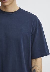 Navy blue short-sleeve t-shirt in soft cotton, featuring a minimalist embroidered logo on the chest and a classic round neckline.