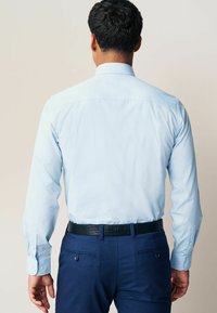 Chemise à manches longues bleu clair avec un col standard, associée à un pantalon bleu marine et une ceinture noire texturée, avec des poignets à boutons.