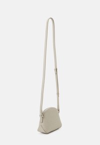 Malá béžová crossbody taška s nastavitelným popruhem a opakujícím se vzorem loga "CK", stojící vzpřímeně na bílém pozadí.
