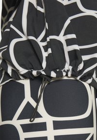Schwarz-weißer gemusterter Oberteil mit geraffter Taille und Zugbanddetail, aus glattem Stoff mit abstrakten Formen in kontrastierenden Farben.