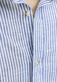 Camisa a rayas azul y blanca con cierre de botones. La tela parece ligera y texturizada, con rayas verticales y un cuello.