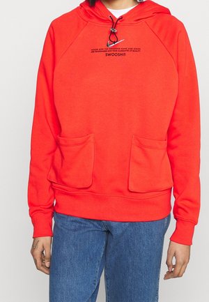 Sweat à capuche rouge vif avec deux poches frontales, cordon noir réglable, et petit texte noir au-dessus de la poitrine indiquant "SWOOSH", porté avec un jean bleu.