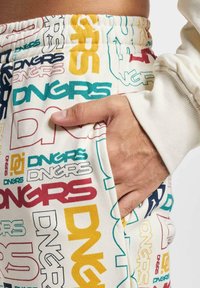 White sweatpants featuring a repeated logo pattern in various colors, with an elastic waistband and side pockets.