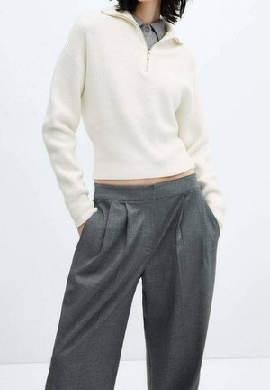 Un pull zippé à côtes blanches associé à un pantalon large à plis gris. Le pull a un col montant ; le tissu semble doux et texturé.