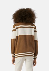 Maglione a coste marrone con strisce horizontal bianche. Design ampio con maniche lunghe e bordi rigati all'orlo e ai polsi.