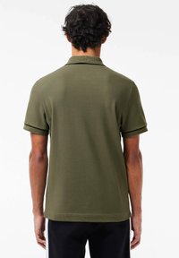 Camisa polo verde oliva de manga corta, con un color clásico y puños de manga enrollados. Tejido suave con un dobladillo recto.