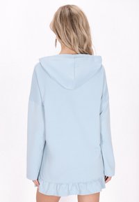 Vaaleansininen hupparimekko, jossa on pitkät hihat, röyhelöhelma ja nyörillä säädettävä huppu. Sileä kangas, rento malli ja sivuaukot.