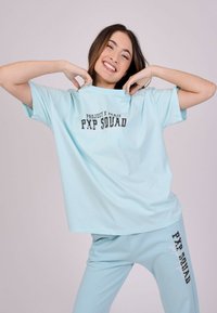 Una camiseta de color azul claro y pantalones a juego presentan "PXP SQUAD" en letras negras y en negrita. Hechos de tela suave, con mangas cortas y un corte relajado.