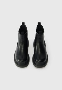 Črne usnjene gležnjarje z elastiko na straneh in zankami za nošenje. Okrogel prst in debel gumijast podplat, gladka tekstura, minimalističen dizajn.