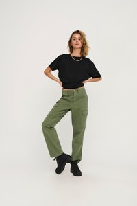Sort cropped t-shirt med korte ærmer, parret med olivengrønne cargo-bukser med sidelommer. Modellen har sorte snørebåndsstøvler på.