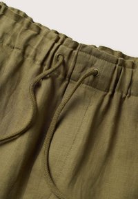 Oliwkowe lniane szorty z elastycznym pasem na gumkę i sznurkiem do regulacji, prezentujące gładką, teksturowaną powierzchnię oraz prosty design.