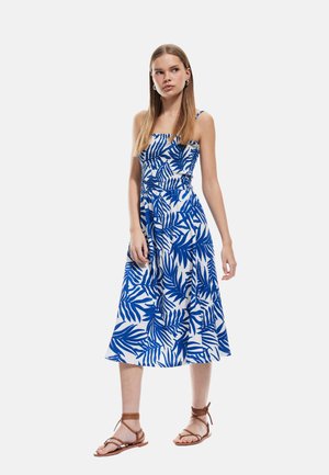 Blue and white floral-printed dress with a fitted bodice, elastic waistband, and a flowing mid-length skirt. Worn with brown strappy sandals.