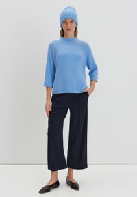 Maglione a coste blu chiaro con maniche a 3/4, abbinato a pantaloni larghi scuri e ballerine nere. Presenta anche un berretto blu coordinato.