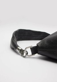 Czarny skórzany pasek torby o teksturowanym wykończeniu, metalowy zamek i gładki, zaokrąglony kształt. Zbliżenie podkreślające materiał i elementy metalowe.