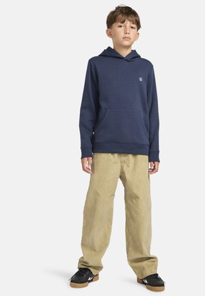 Marineblauwe hoodie met een voorzak en logo, gecombineerd met lichtbeige wijde corduroypants. Zwarte sneakers met een gumrubberen zool.
