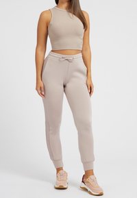 Hellbeige, kurz geschnittenes Tanktop mit gerippter Textur, kombiniert mit passenden, schmal zulaufenden Jogginghosen mit Kordelzug und seitlichen Taschen.