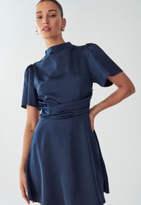 Navy blue satin dress with short puff sleeves, high neckline, and a cinched waist, falling to a flared hem with a smooth texture.