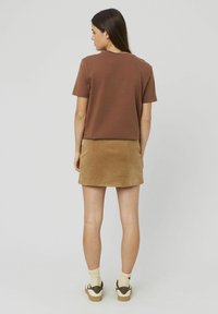 T-shirt marron à manches courtes associé à une mini-jupe en velours côtelé beige. Le mannequin porte des chaussettes claires et des baskets avec une semelle texturée.